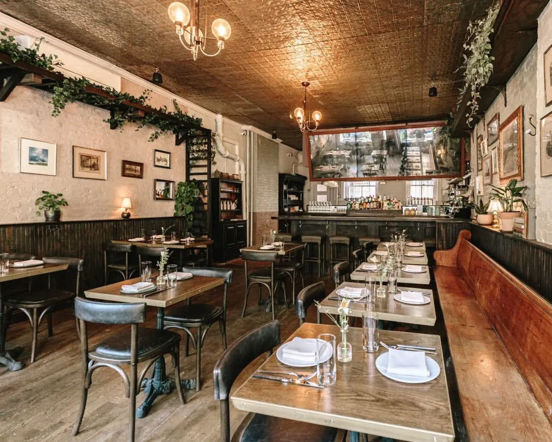 Dining room at Clover Hill with banquette seating, bentwood chairs, framed pictures and trailing greenery
