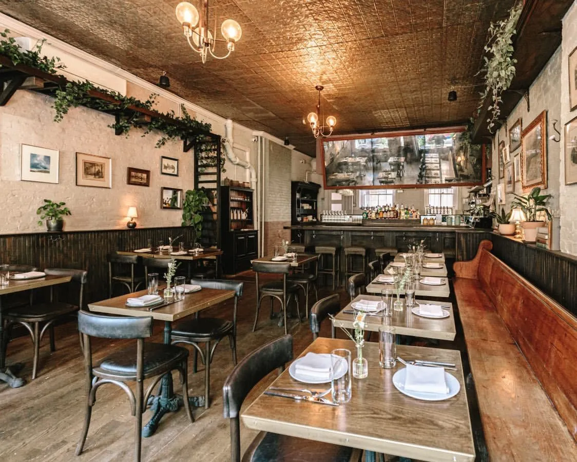 Dining room at Clover Hill with banquette seating, bentwood chairs, framed pictures and trailing greenery