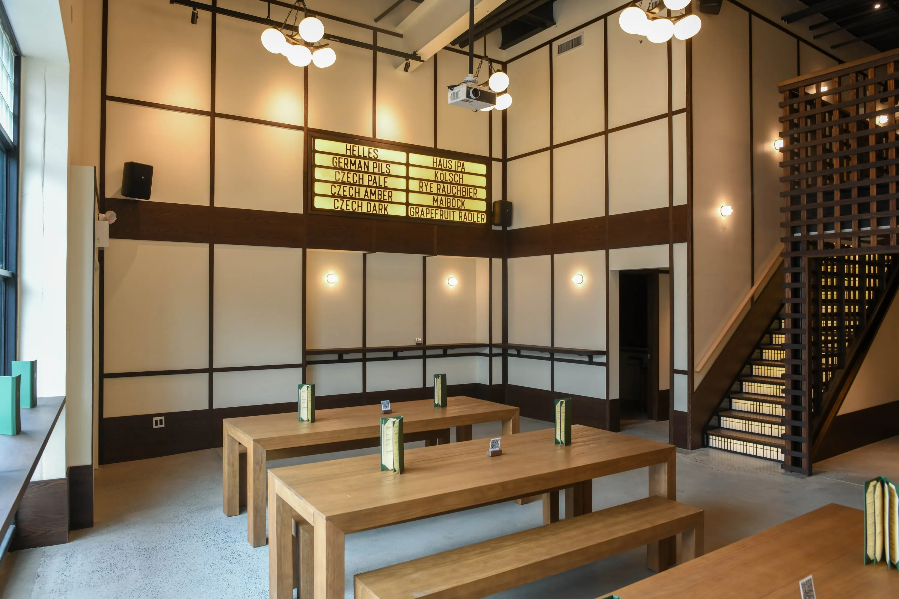 Eckhart Beer Co beer hall with long communal tables, timber lattice stair and tall gridded windows