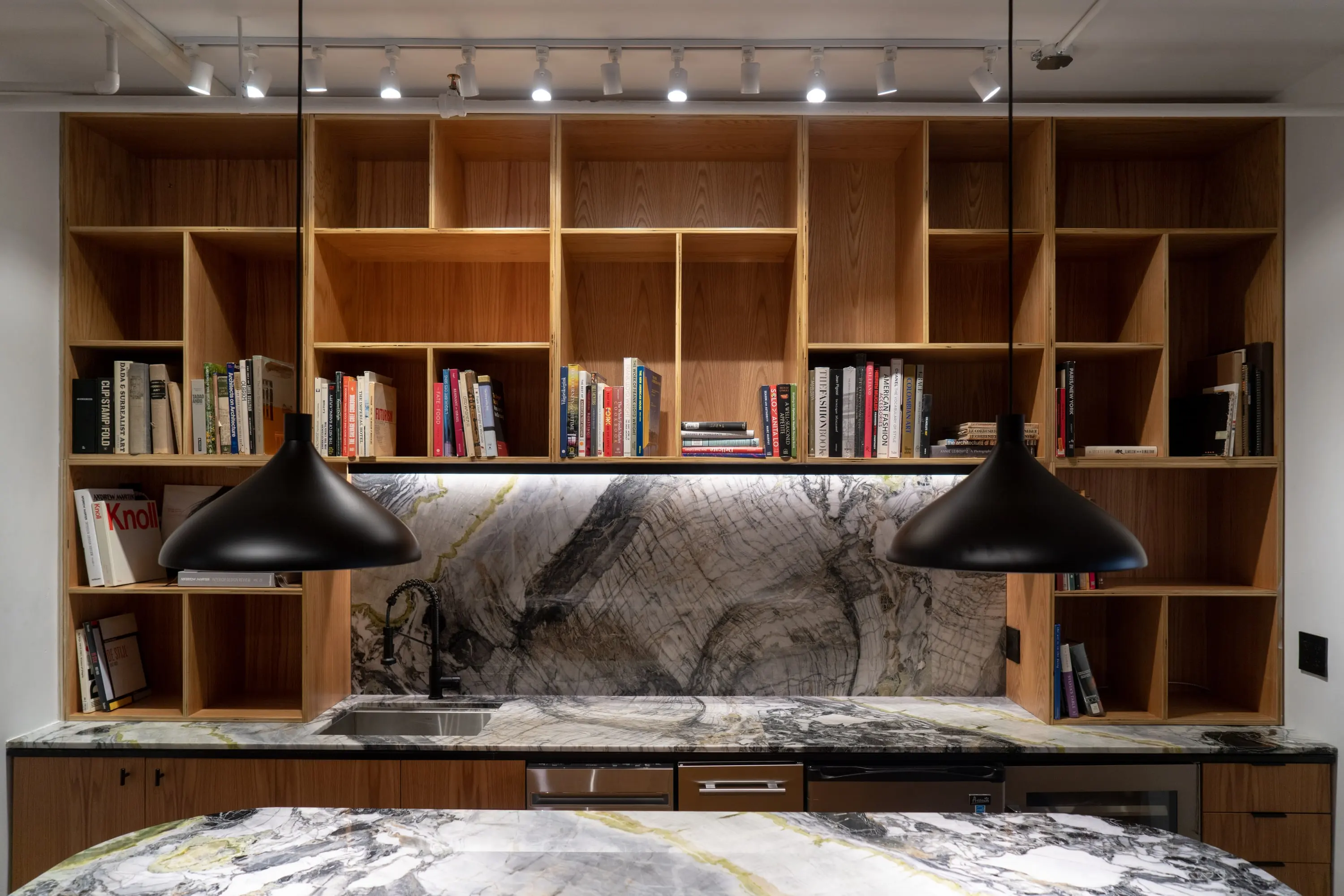 Library bar at KZ_K Studio with a marble island, plywood shelving full of books and black pendants