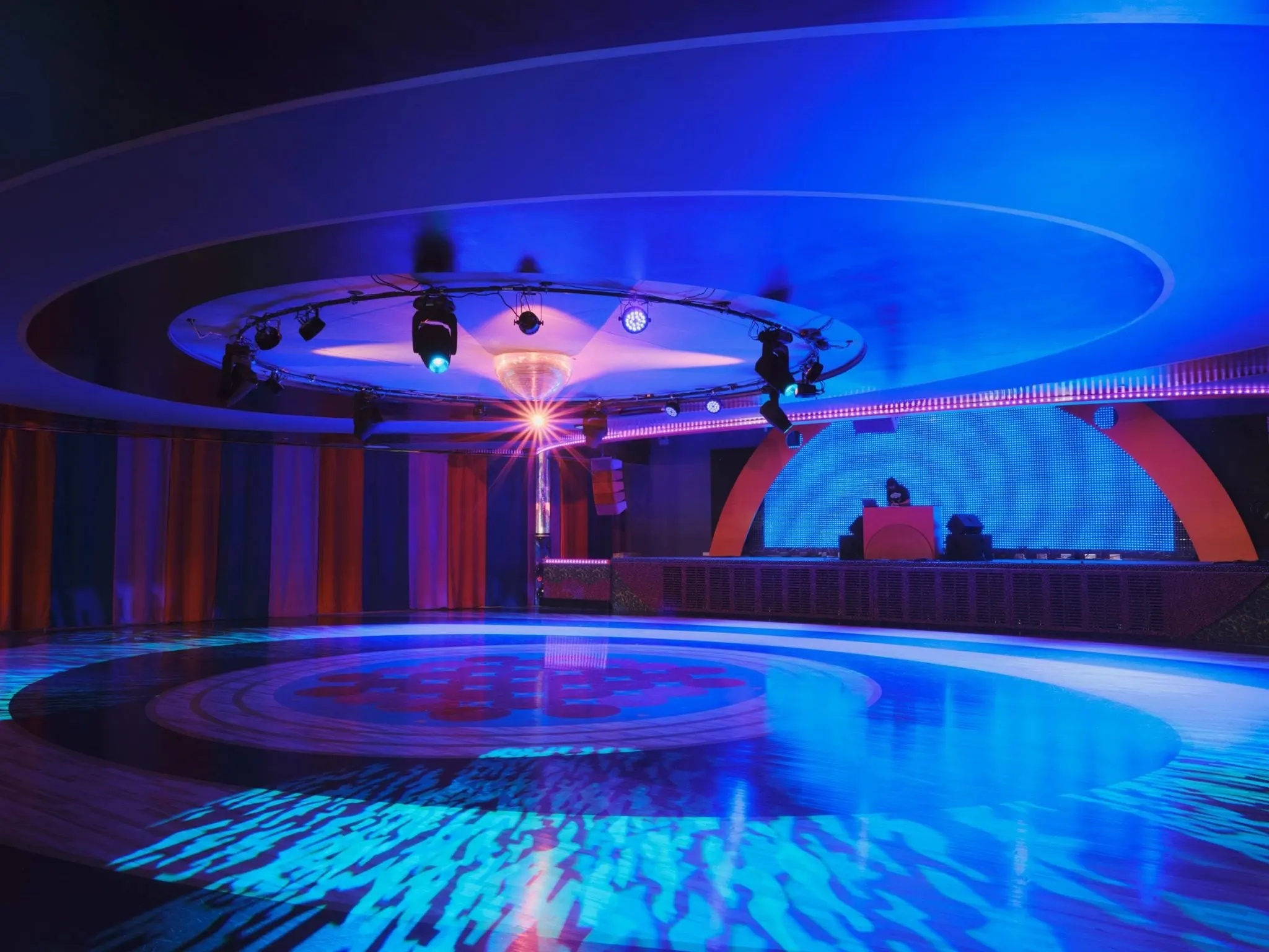 Xanadu roller rink under blue light with a DJ booth and layered ceiling coves