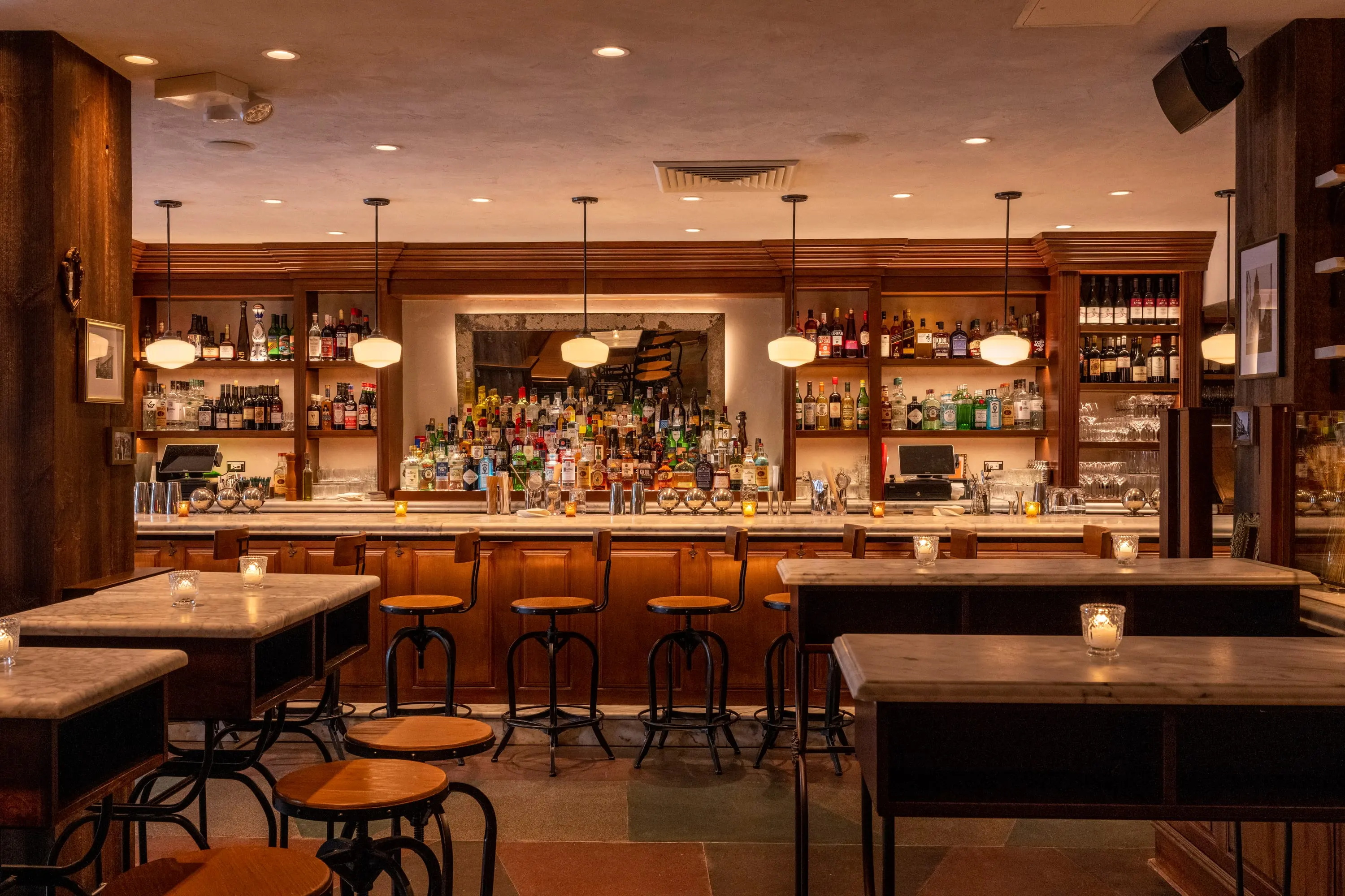 The bar at One Fifth with marble top, wood stools and a lit back bar
