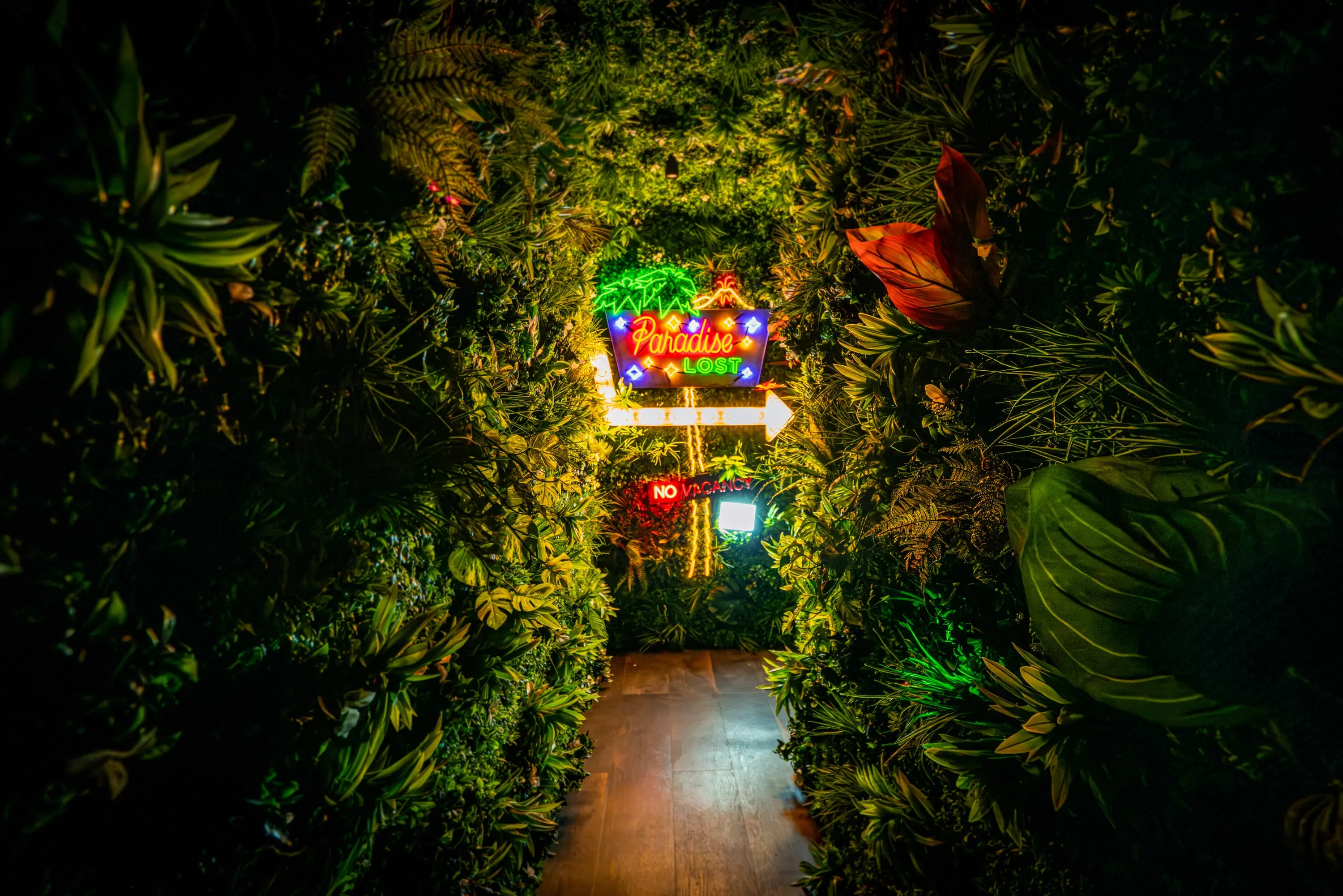 Entry tunnel at Paradise Lost lined with dense green foliage and glowing neon at the far end
