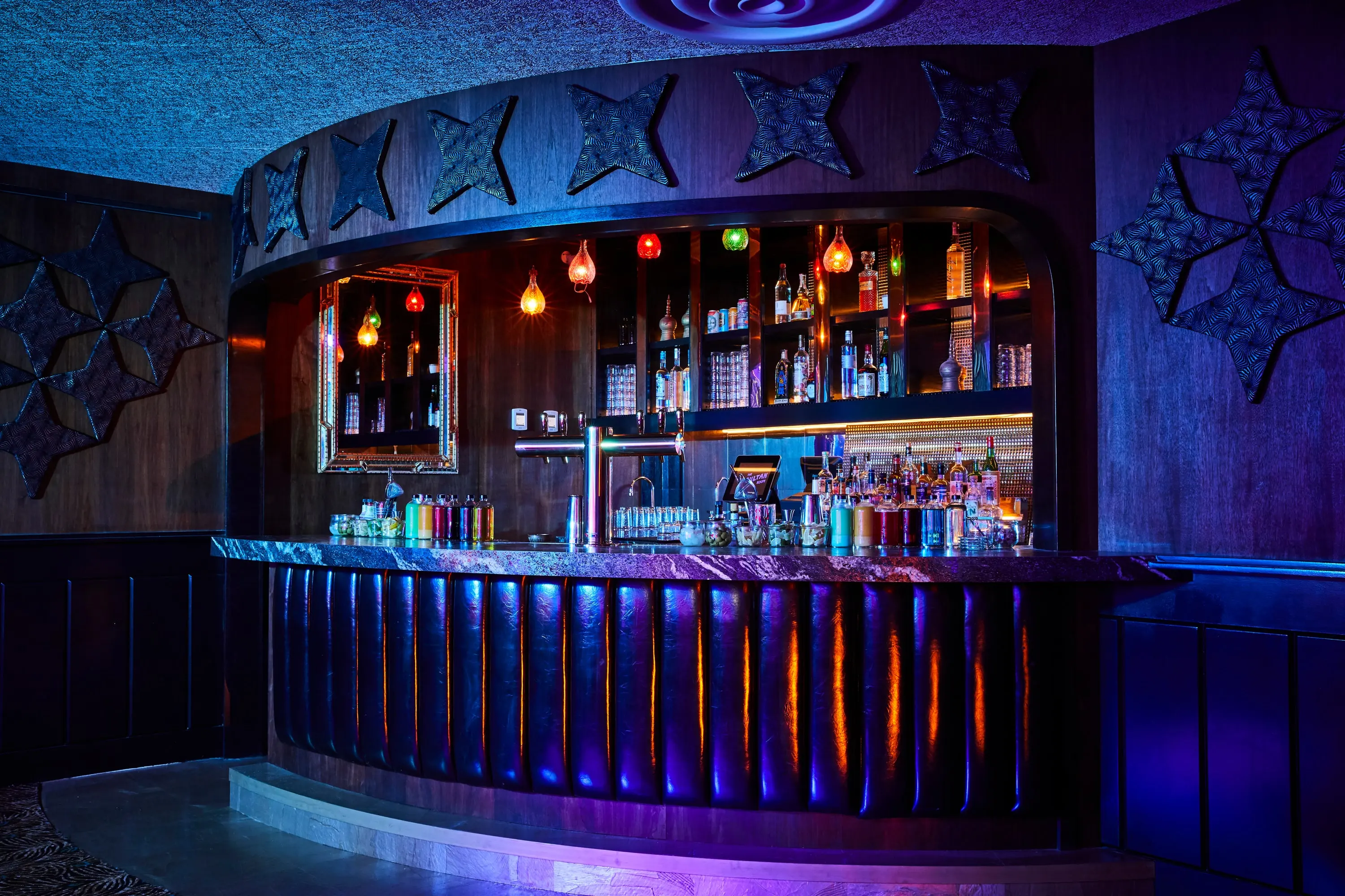 Curved bar at The Sultan Room under blue and violet light with carved timber panels