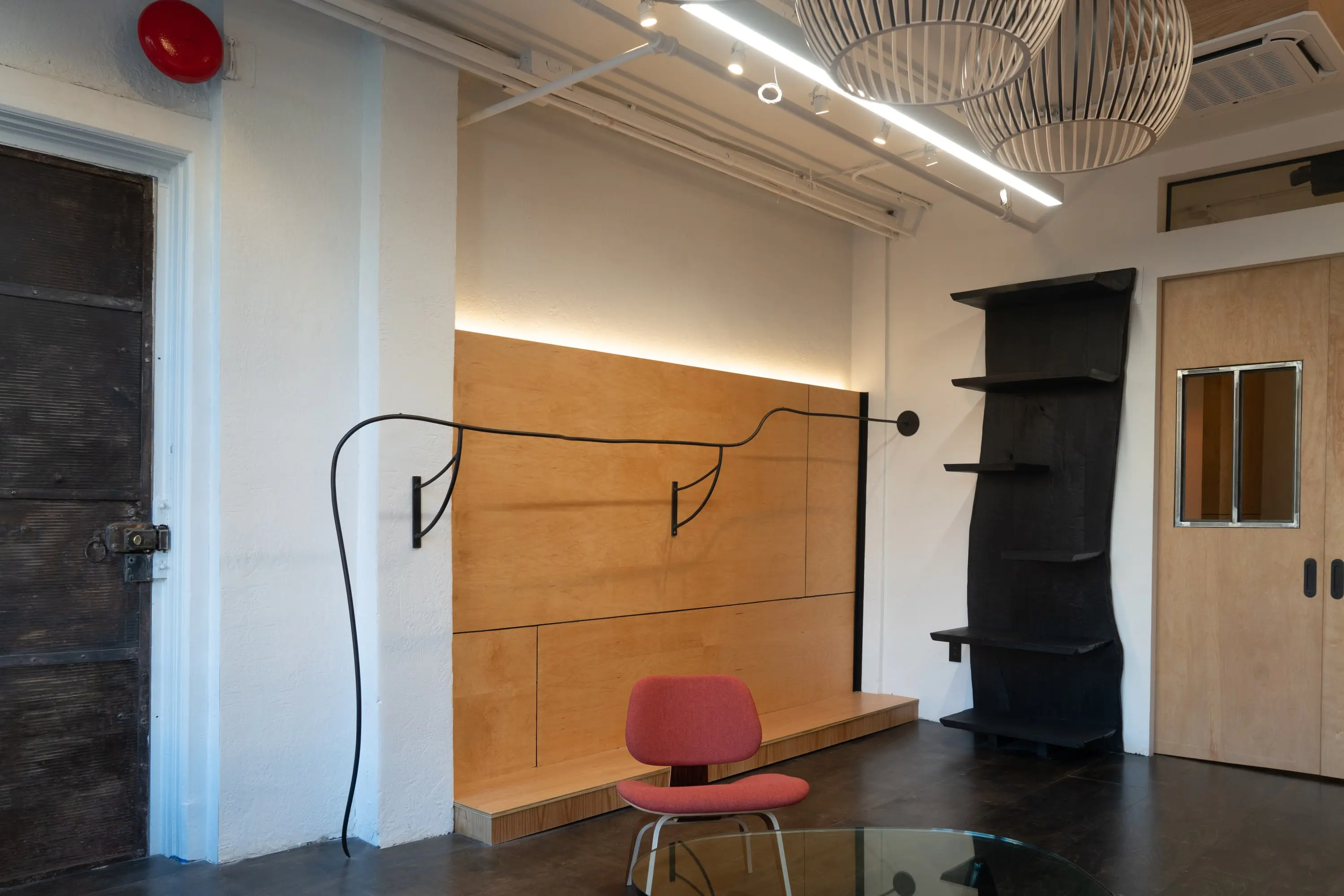 Birch plywood wall at KZ_K Studio with a bent-steel hook rail, red chair and charred column