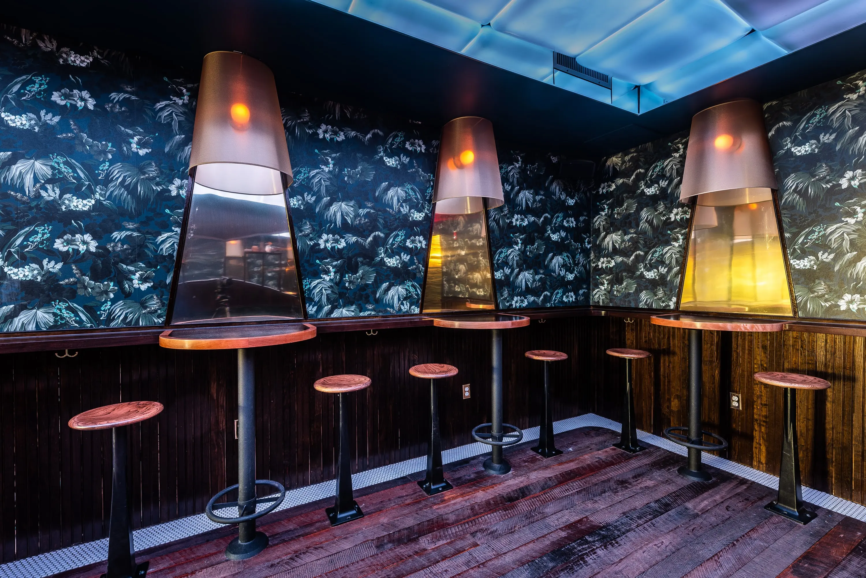 High tables against a patterned wall with conical pendant lights at No Kisses