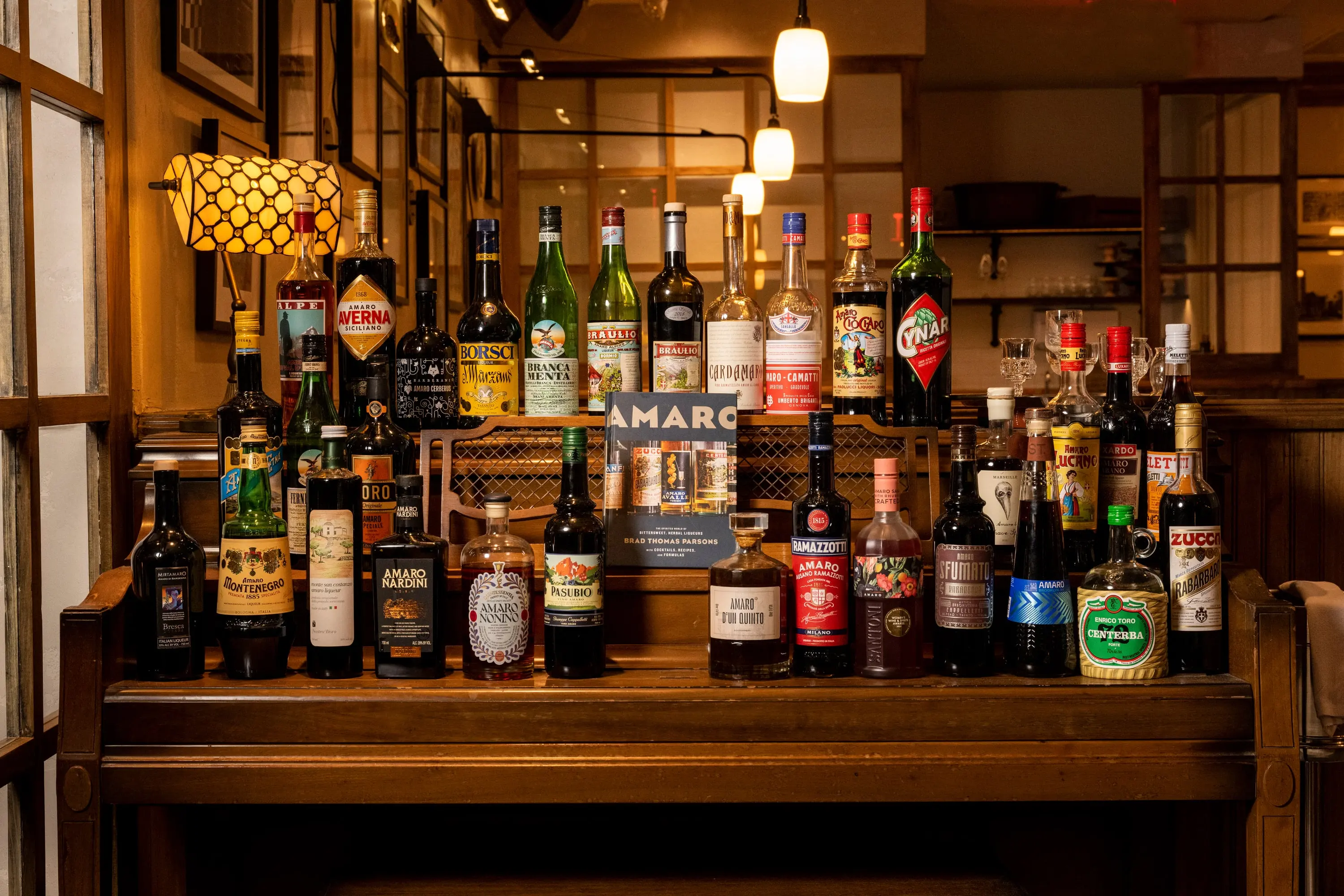 Amaro back bar at One Fifth with rows of bottles under a brass lamp