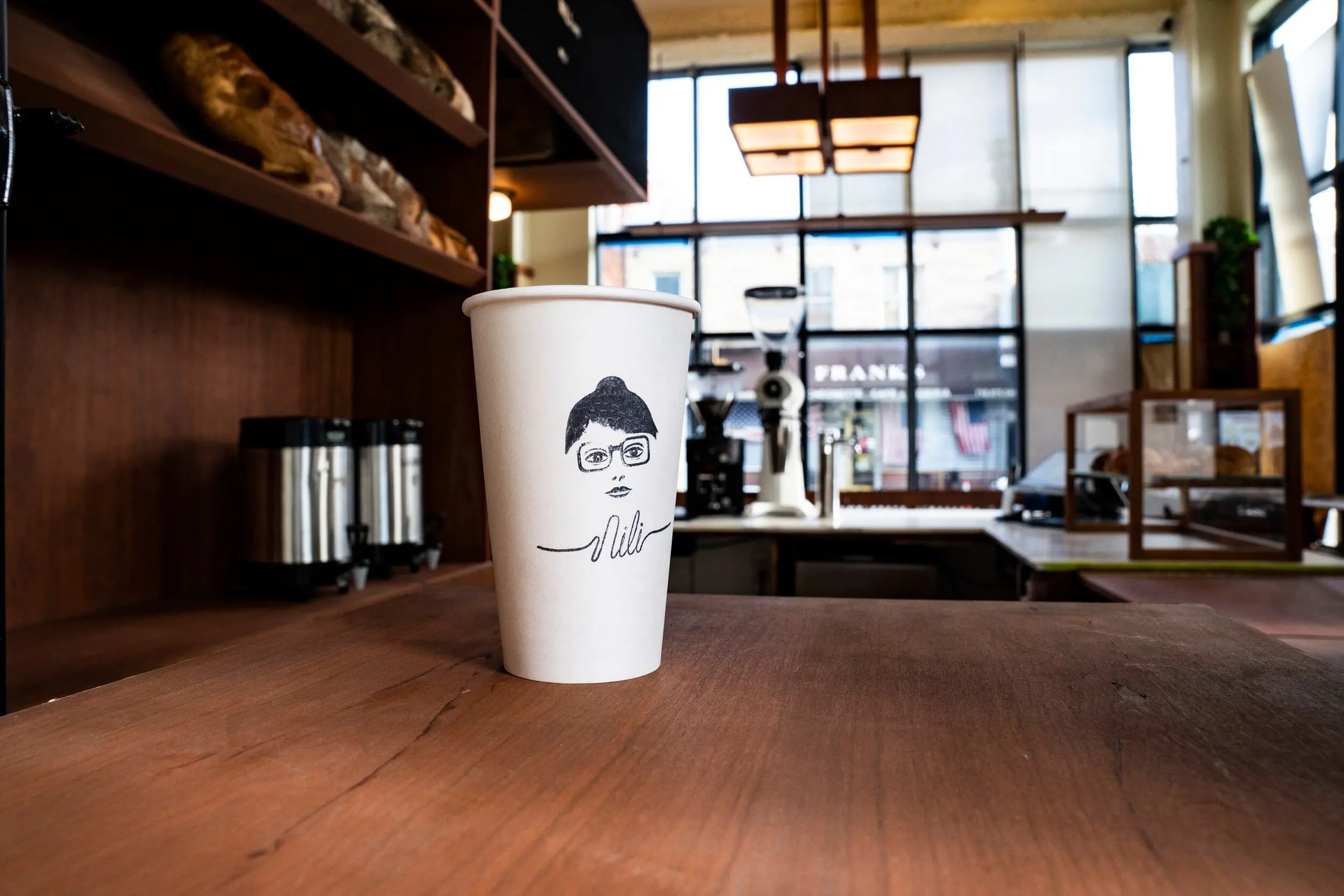 Branded paper cup on the walnut counter at Nili with the bar in the background