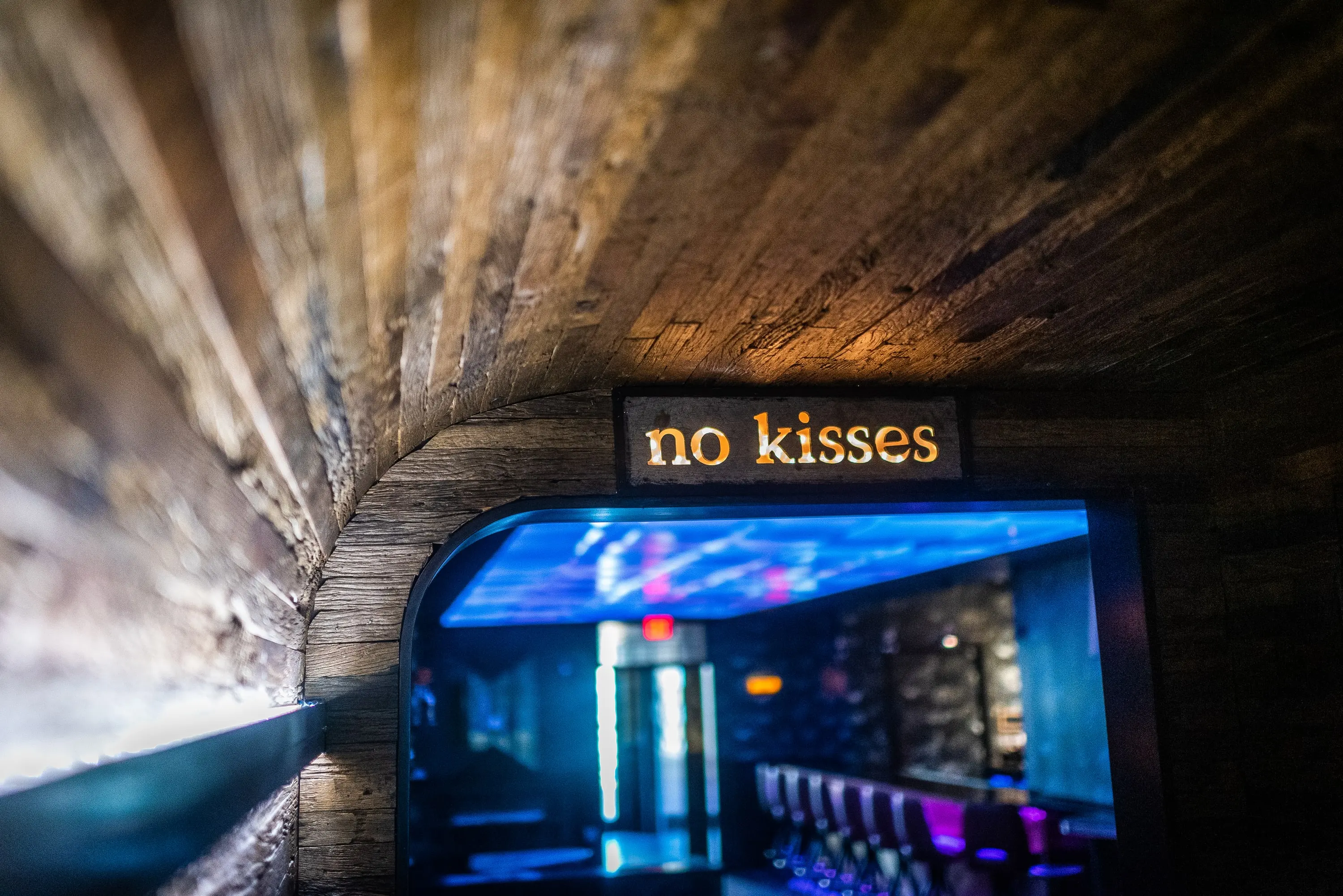 Brick tunnel entrance leading into No Kisses, sign glowing at the far end