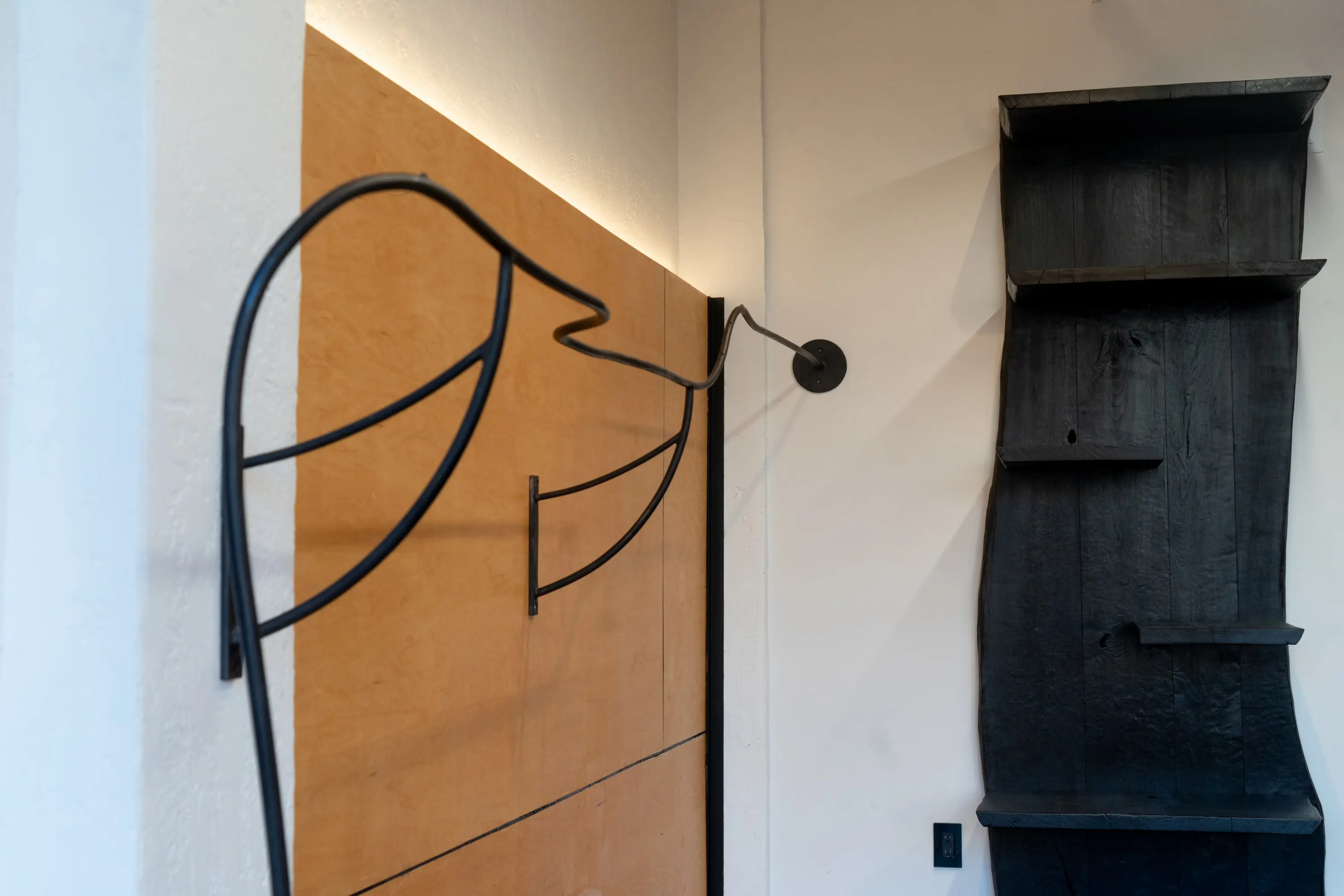 Bent-steel hook and charred timber shelf on a plywood wall at KZ_K Studio