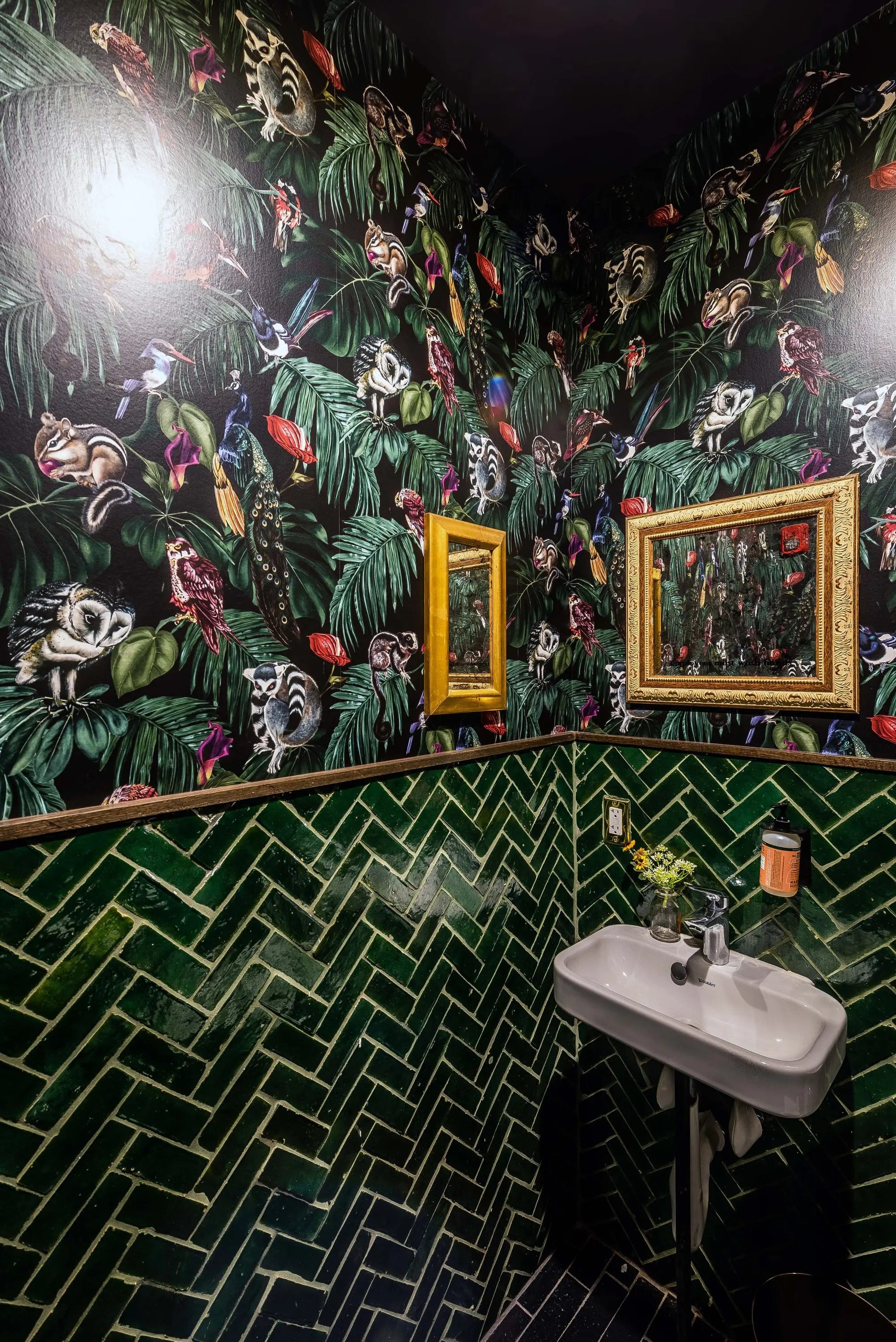 Restroom at No Kisses with jungle-print wallpaper and green herringbone tile