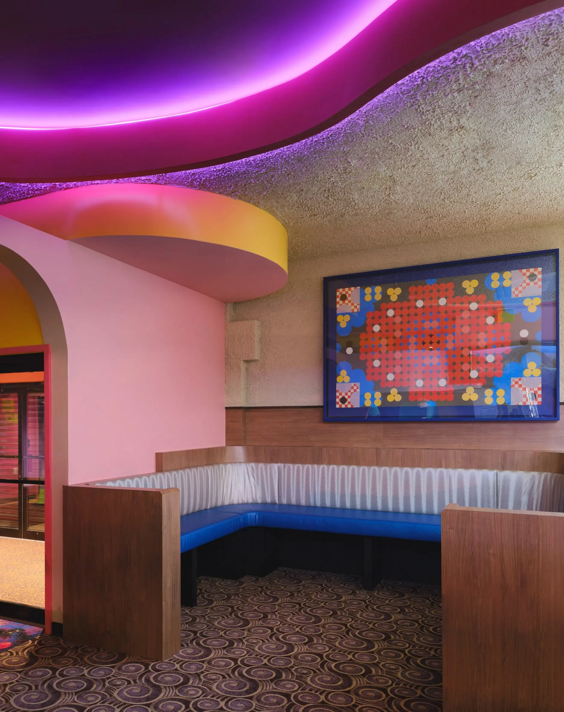Corner banquette at Xanadu with a pixel-art wall panel and pink ceiling cove