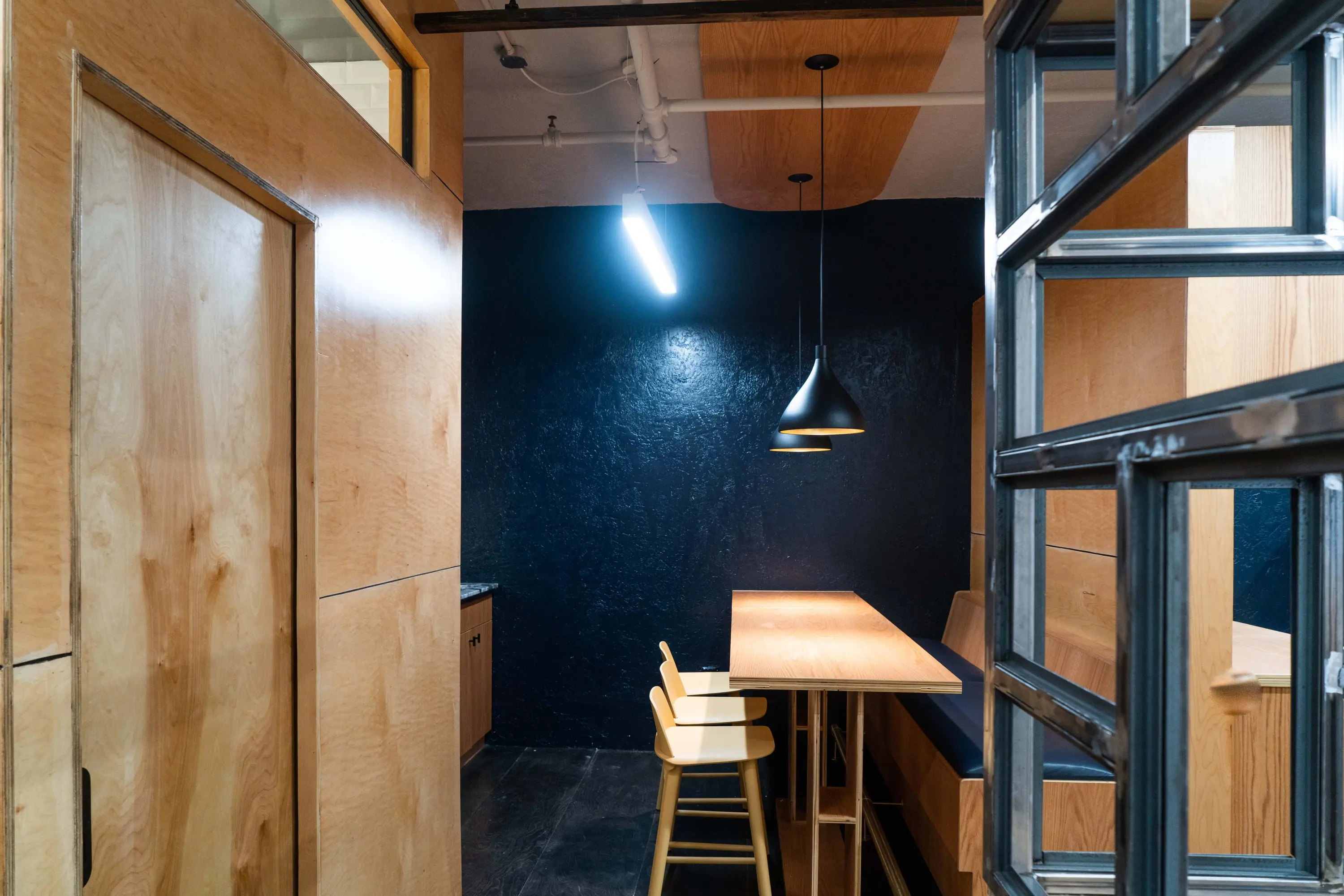 Work nook at KZ_K Studio with a plywood counter, black wall and steel-framed glazing