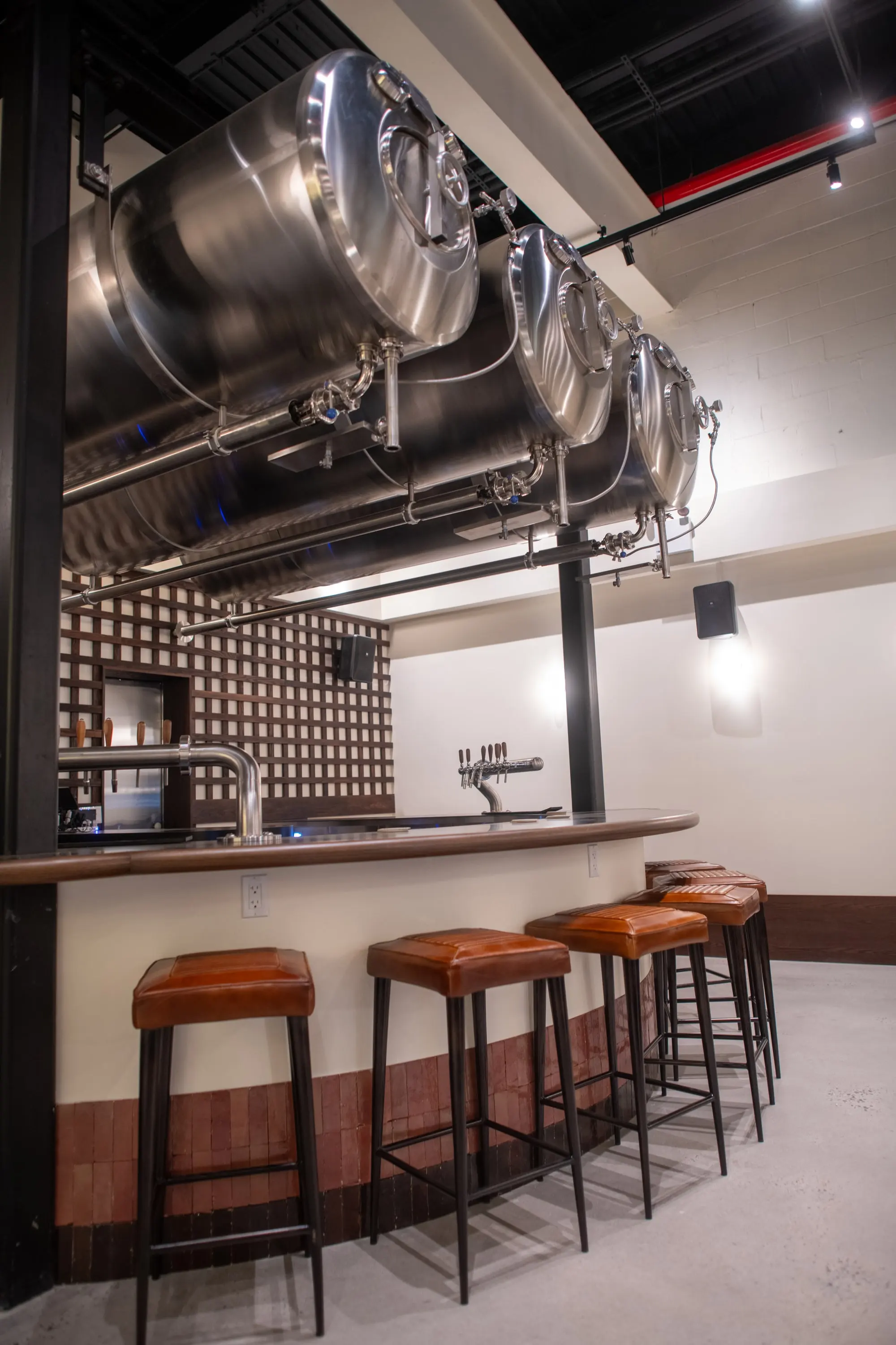 Bar at Eckhart Beer Co with leather stools and brewery tanks visible overhead