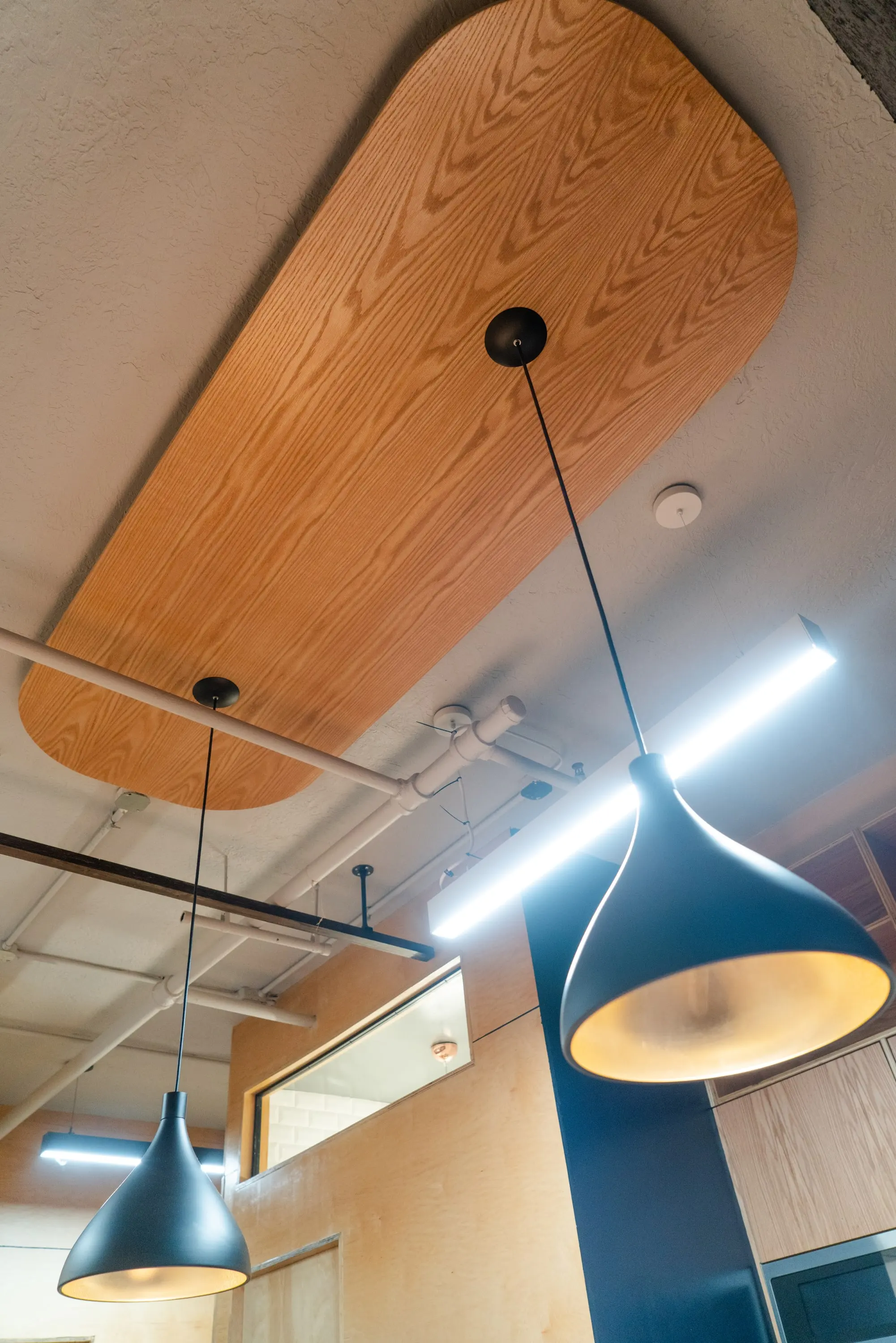 Black pendant lamps hanging from a plywood ceiling panel at KZ_K Studio